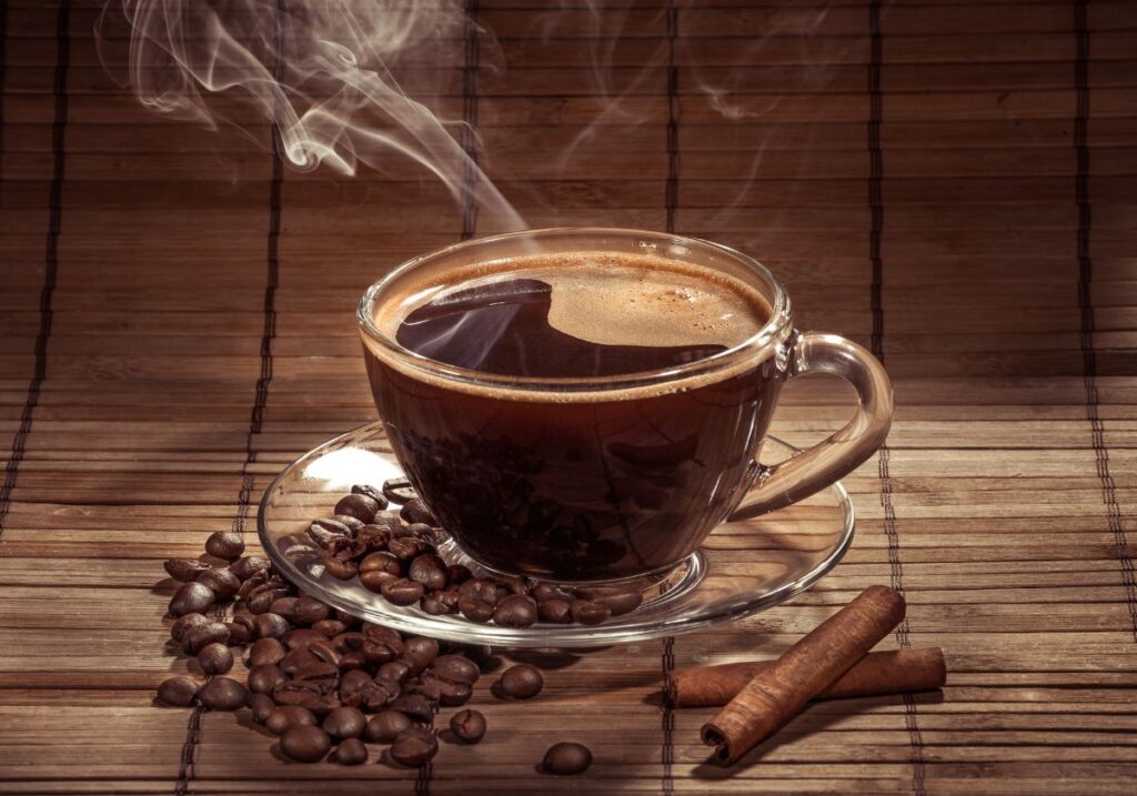 A steaming cup of black coffee with a few coffee beans a cinnamon sticks